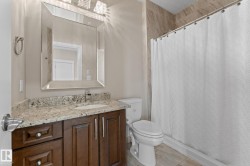 Bathroom featuring a dark wood vanity with a granite countertop and undermount sink, an illuminated framed mirror, a tiled shower surround, and tile flooring - 