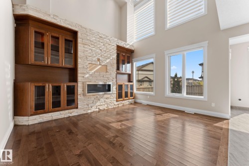 Spacious living area featuring wood-finish flooring, a stacked stone accent wall, and built-in wood cabinetry with glass fronts - 16543 132 Street, Edmonton, AB - Indoor With Fireplace