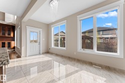 Spacious area featuring large format tile flooring, extensive natural light from multiple windows, a white paneled door with glass insert, and a contemporary chandelier - 