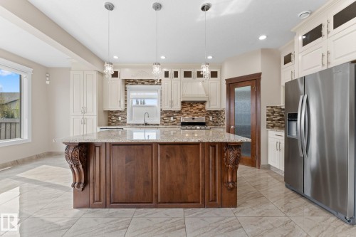 Spacious kitchen featuring a large central island with carved corbels, granite-style countertop, and pendant lighting - 16543 132 Street, Edmonton, AB - Indoor Photo Showing Kitchen With Upgraded Kitchen