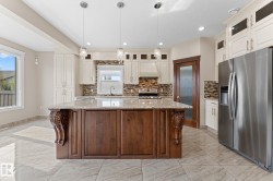Spacious kitchen featuring a large central island with carved corbels, granite-style countertop, and pendant lighting - 