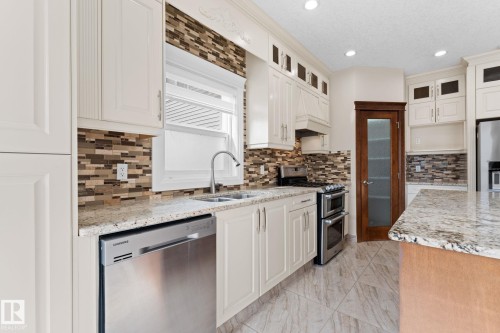 Kitchen featuring granite countertops, stainless steel appliances, a mosaic tile backsplash, white cabinetry, and wood-finish flooring - 16543 132 Street, Edmonton, AB - Indoor Photo Showing Kitchen With Double Sink With Upgraded Kitchen