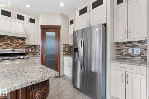 Gourmet kitchen featuring a stainless steel refrigerator, white cabinetry, granite countertops, a tiled backsplash, and wood-finish flooring - 16543 132 Street, Edmonton, AB - Indoor Photo Showing Kitchen With Upgraded Kitchen