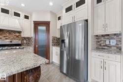 Gourmet kitchen featuring a stainless steel refrigerator, white cabinetry, granite countertops, a tiled backsplash, and wood-finish flooring - 