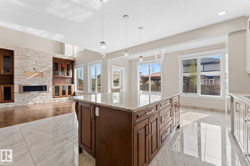 Expansive kitchen island with a light granite countertop and rich wood-finish cabinetry - 16543 132 Street, Edmonton, AB - Indoor Photo Showing Kitchen With Fireplace
