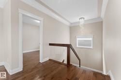 Hardwood flooring extends throughout this upper-level space, featuring a modern glass and wood handrail, recessed ceiling with crown molding, and an elegant crystal chandelier - 