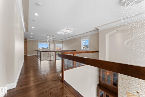 Open concept upper hallway featuring wood-finish flooring, glass panel railings with dark wood handrails, recessed lighting, and a prominent crystal chandelier - 16543 132 Street, Edmonton, AB - Indoor Photo Showing Other Room