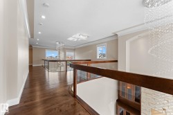 Open concept upper hallway featuring wood-finish flooring, glass panel railings with dark wood handrails, recessed lighting, and a prominent crystal chandelier - 