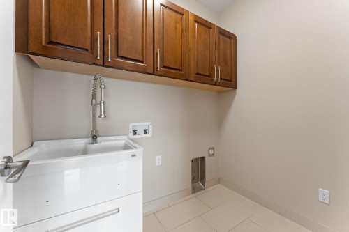 Utility room featuring a large white basin sink with a chrome pull-down faucet, upper wood-finish cabinetry, and light-toned tile flooring - 16543 132 Street, Edmonton, AB - Indoor