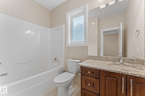 Bathroom featuring a white tub and shower surround, a white toilet, a window with frosted glass, a wooden vanity with a stone countertop, and a chrome faucet - 16543 132 Street, Edmonton, AB - Indoor Photo Showing Bathroom