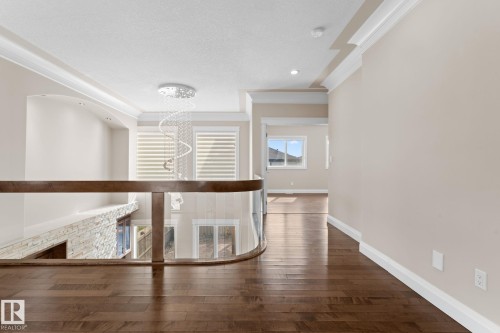 Upper-level hallway featuring hardwood flooring, crown molding, a decorative chandelier, and a curved glass railing - 16543 132 Street, Edmonton, AB - Indoor Photo Showing Other Room