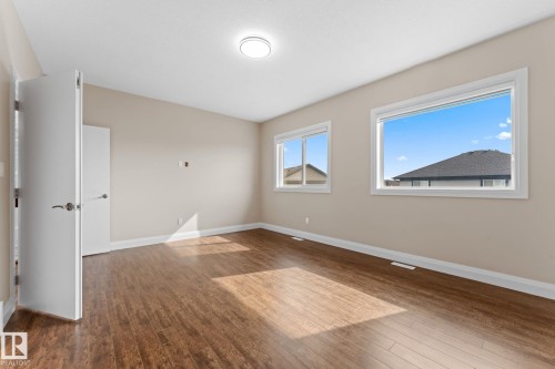 Spacious room featuring wood-finish flooring, two large windows, a flush-mount ceiling light fixture, and neutral-toned walls - 16543 132 Street, Edmonton, AB - Indoor Photo Showing Other Room