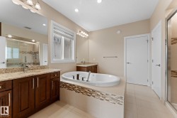 Bathroom featuring a jetted soaking tub, double vanity with granite countertops, and a glass-enclosed shower with tiled accents - 