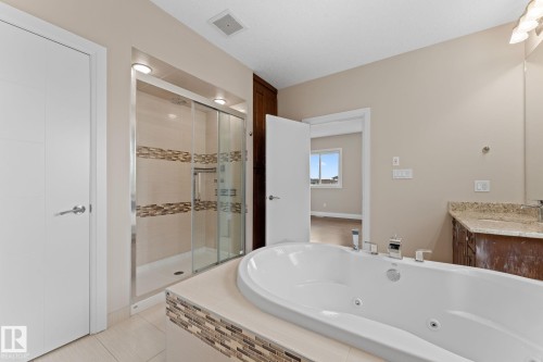 Bathroom featuring a white jetted soaking tub, a glass-enclosed shower with tiled accents, and a vanity with a stone countertop - 16543 132 Street, Edmonton, AB - Indoor Photo Showing Bathroom