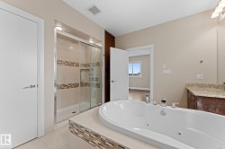 Bathroom featuring a white jetted soaking tub, a glass-enclosed shower with tiled accents, and a vanity with a stone countertop - 