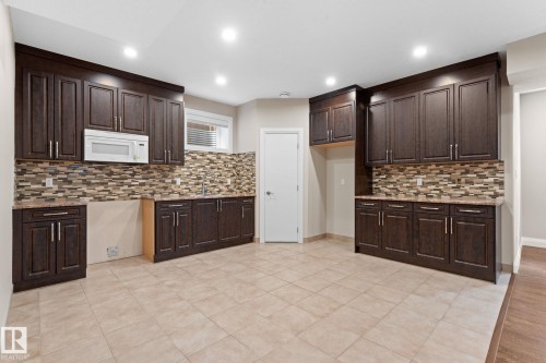 Kitchen featuring dark wood-finish cabinetry, a microwave, and a multi-tone tile backsplash - 16543 132 Street, Edmonton, AB - Indoor Photo Showing Kitchen With Upgraded Kitchen