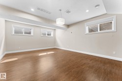 Spacious room featuring rich wood-finish flooring, recessed lighting, and a modern drum pendant fixture - 