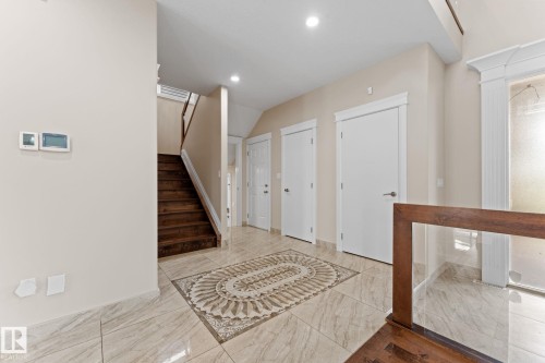 Foyer featuring large format tile flooring with decorative inlay, a wood staircase, and multiple white panel doors - 16543 132 Street, Edmonton, AB - Indoor Photo Showing Other Room