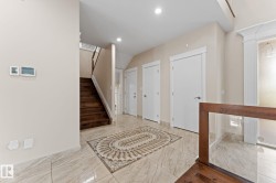 Foyer featuring large format tile flooring with decorative inlay, a wood staircase, and multiple white panel doors - 