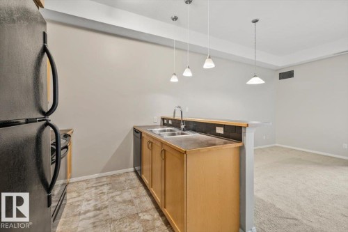 Kitchen area featuring light wood cabinetry, a dual basin stainless steel sink, and a black subway tile backsplash - 228 10531 117 Street, Edmonton, AB - Indoor Photo Showing Kitchen With Double Sink