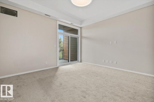 Spacious room featuring neutral carpeting and a sliding glass door leading to a private balcony - 228 10531 117 Street, Edmonton, AB - Indoor Photo Showing Other Room