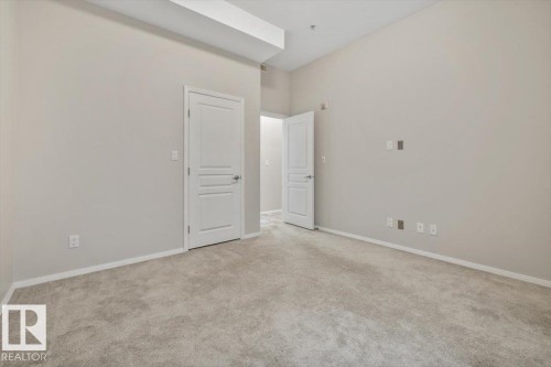 Spacious room featuring plush gray carpeting, crisp white trim, and a soaring vaulted ceiling - 228 10531 117 Street, Edmonton, AB - Indoor Photo Showing Other Room