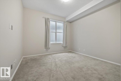 Carpeted room featuring a double-paned window with privacy glass, light gray wall paint, white trim, and a flush-mount ceiling light fixture - 228 10531 117 Street, Edmonton, AB - Indoor Photo Showing Other Room