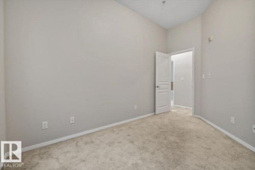 Carpeted room featuring light gray walls, white baseboards, and a white interior door with contemporary hardware - 228 10531 117 Street, Edmonton, AB - Indoor Photo Showing Other Room