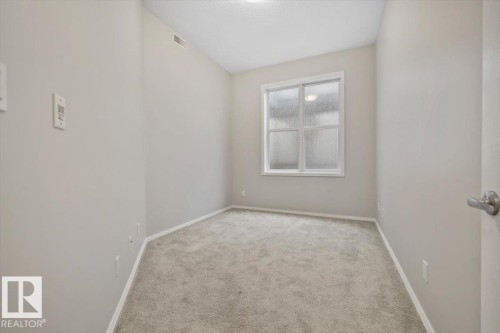 Neutral-toned walls and carpeted flooring define this room, featuring a white-framed window - 228 10531 117 Street, Edmonton, AB - Indoor Photo Showing Other Room