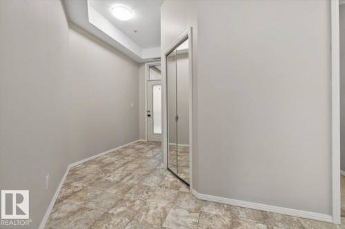 Tiled entryway featuring a white entry door with frosted glass panel, recessed ceiling lighting, and a mirrored closet - 228 10531 117 Street, Edmonton, AB - Indoor Photo Showing Other Room