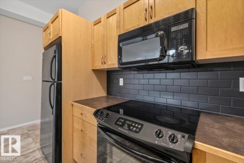 Well-appointed kitchen featuring light wood cabinetry, black subway tile backsplash, and dark countertops - 228 10531 117 Street, Edmonton, AB - Indoor Photo Showing Kitchen