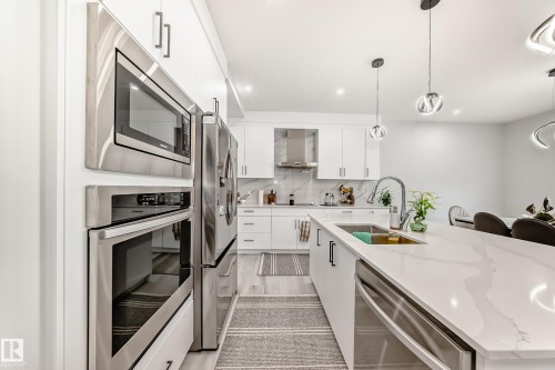 Modern kitchen featuring stainless steel appliances, white cabinetry, a large kitchen island with a sink, and pendant lighting - 4509 170A Avenue, Edmonton, AB - Indoor Photo Showing Kitchen With Stainless Steel Kitchen With Upgraded Kitchen