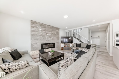 Living area featuring light-toned flooring, a gray tiled accent wall with an integrated fireplace, and a staircase with white railings - 4509 170A Avenue, Edmonton, AB - Indoor Photo Showing Living Room With Fireplace
