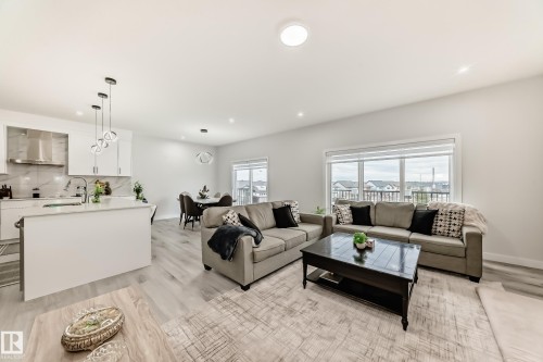 The open concept living area features light-toned flooring, a kitchen with white cabinetry and a stainless steel range hood, and a dining area with a modern light fixture - 4509 170A Avenue, Edmonton, AB - Indoor Photo Showing Living Room