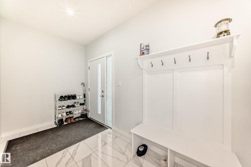 Entryway featuring white tile flooring, a white built-in storage unit with hooks and shelving, and a bright white door with frosted glass panels - 4509 170A Avenue, Edmonton, AB - Indoor Photo Showing Other Room