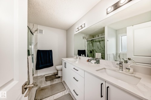 This bathroom features a double vanity with white cabinetry and dark hardware, a large mirror, and overhead lighting - 4509 170A Avenue, Edmonton, AB - Indoor Photo Showing Bathroom