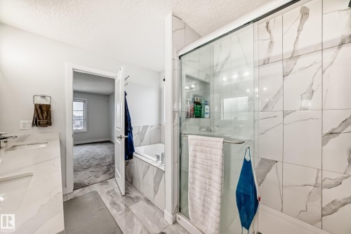 This bathroom features white marble-effect tiling on the walls and floor, a built-in bathtub, and a glass-enclosed shower - 4509 170A Avenue, Edmonton, AB - Indoor Photo Showing Bathroom