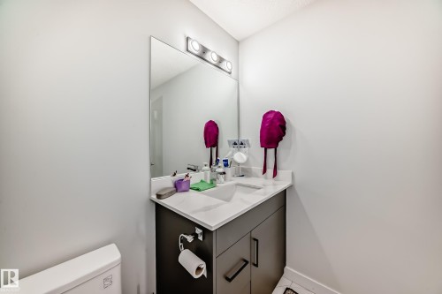 Bathroom featuring a vanity with a white countertop and dark cabinetry, a mirror with overhead lighting, and a toilet - 4509 170A Avenue, Edmonton, AB - Indoor Photo Showing Bathroom