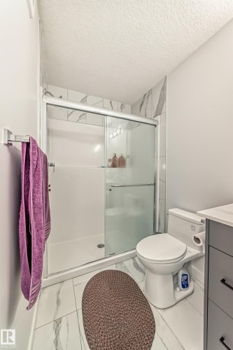 The bathroom features a shower with sliding glass doors and white tiled walls, a toilet, and a vanity with dark cabinetry and a light-colored countertop - 4509 170A Avenue, Edmonton, AB - Indoor Photo Showing Bathroom