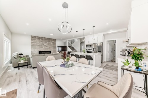 The open concept living area features light-toned flooring, a dining area with a modern chandelier, and a living room with a feature wall fireplace - 4509 170A Avenue, Edmonton, AB - Indoor
