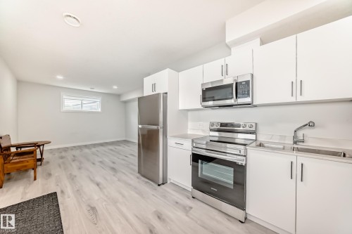The property features a kitchen with white cabinetry, stainless steel appliances including a refrigerator, range, and microwave, and a double basin sink - 4509 170A Avenue, Edmonton, AB - Indoor Photo Showing Kitchen