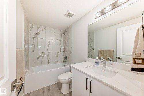 Bathroom featuring a bathtub with tiled surround, a vanity with a white countertop and rectangular sink, and a large mirror - 4509 170A Avenue, Edmonton, AB - Indoor Photo Showing Bathroom