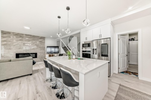 Open concept living space featuring a kitchen island with seating, pendant lighting, stainless steel appliances, and a living room with a fireplace and textured accent wall - 4509 170A Avenue, Edmonton, AB - Indoor Photo Showing Kitchen With Fireplace With Upgraded Kitchen