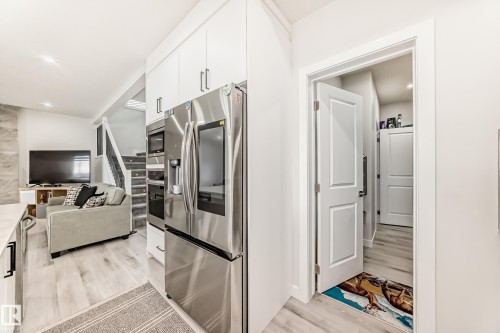 The property features a kitchen with stainless steel appliances and white cabinetry, opening to a living area with light-toned flooring - 4509 170A Avenue, Edmonton, AB - Indoor Photo Showing Other Room