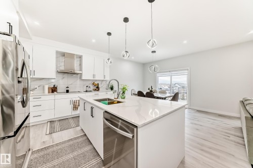 The kitchen features white cabinetry, stainless steel appliances, and a central island with a sink, all beneath modern pendant lighting - 4509 170A Avenue, Edmonton, AB - Indoor Photo Showing Kitchen With Stainless Steel Kitchen With Upgraded Kitchen