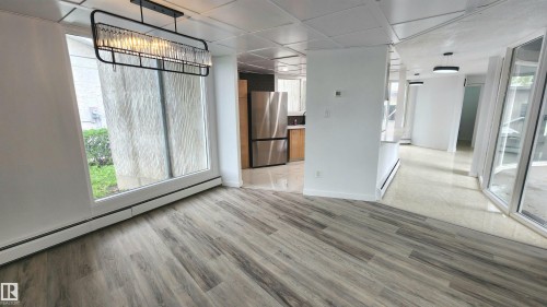 Spacious room with wood-finish flooring, a contemporary linear chandelier, and expansive windows - 9535 147 Avenue, Edmonton, AB - Indoor Photo Showing Other Room