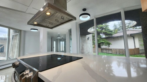 Contemporary kitchen island with an integrated cooktop, a stainless steel range hood, and luminous pendant lighting - 9535 147 Avenue, Edmonton, AB - Indoor Photo Showing Other Room