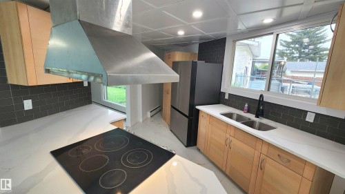 Contemporary kitchen featuring light wood cabinetry, quartz countertops, a black subway tile backsplash, and stainless steel appliances - 9535 147 Avenue, Edmonton, AB - Indoor Photo Showing Kitchen With Double Sink