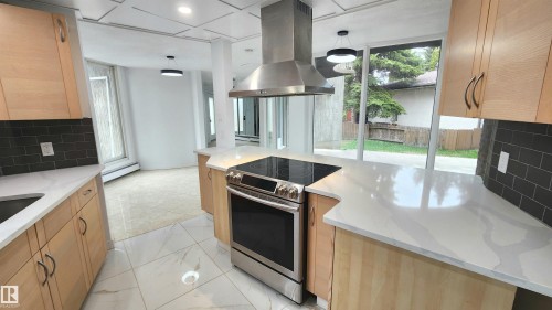 Contemporary kitchen featuring light wood cabinetry, a stainless steel range with overhead hood, dark subway tile backsplash, and light-toned countertops - 9535 147 Avenue, Edmonton, AB - Indoor Photo Showing Kitchen With Upgraded Kitchen