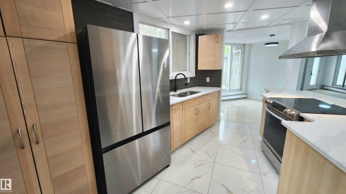 Modern kitchen featuring white marble-look tile flooring, light wood-finish cabinetry, stainless steel appliances, dark subway tile backsplash, and white countertops - 9535 147 Avenue, Edmonton, AB - Indoor Photo Showing Kitchen With Double Sink